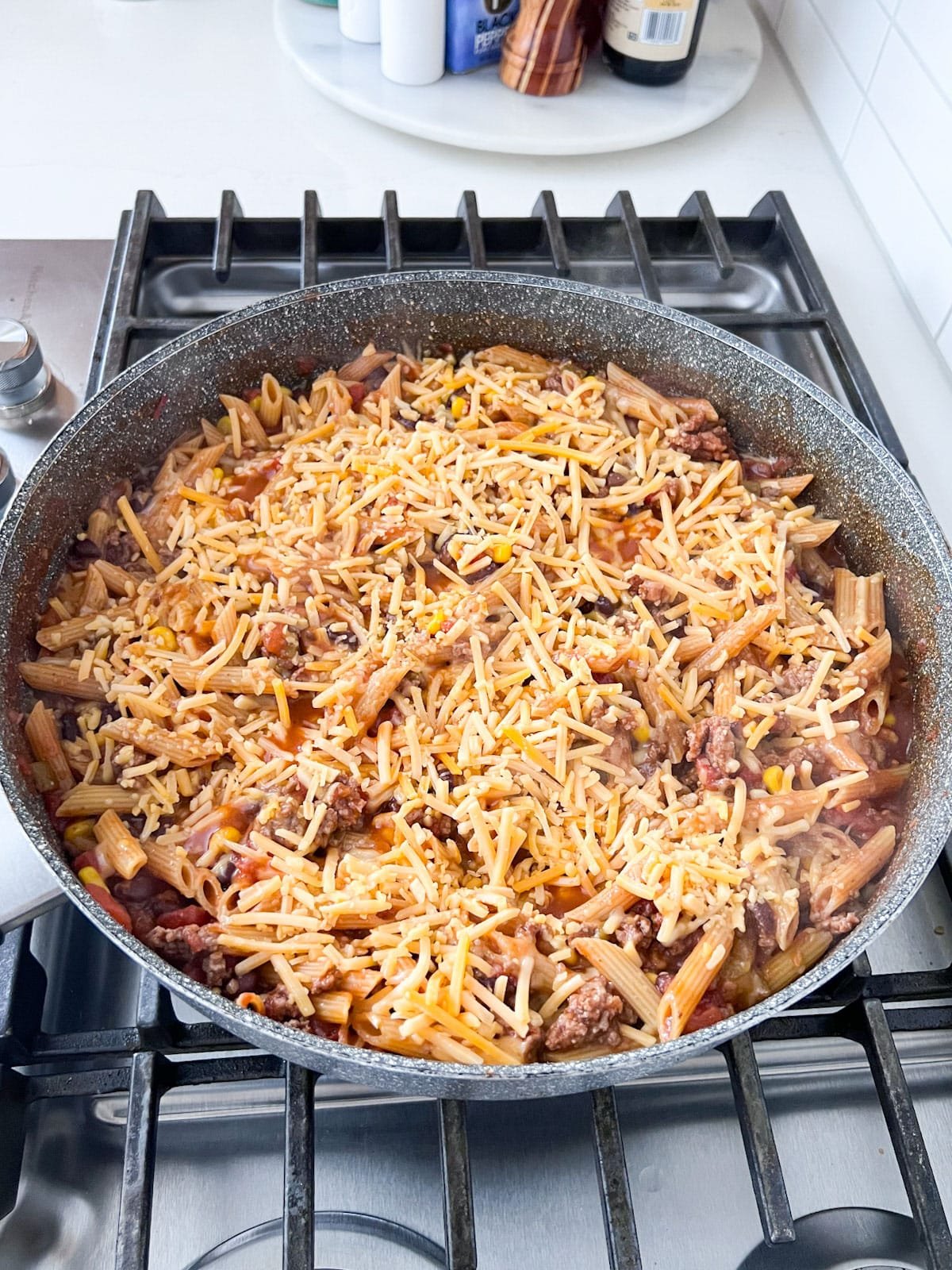 Skillet of one pot taco pasta on a stove with shredded cheese sprinkled on top.