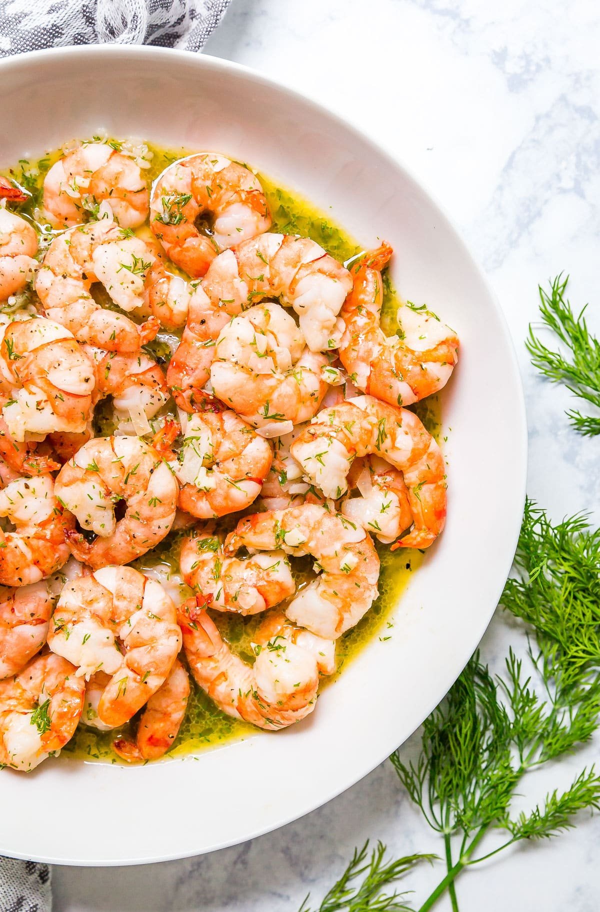 An overhead image of half a white bowl of lemon shrimp with fresh dill next to the bowl.