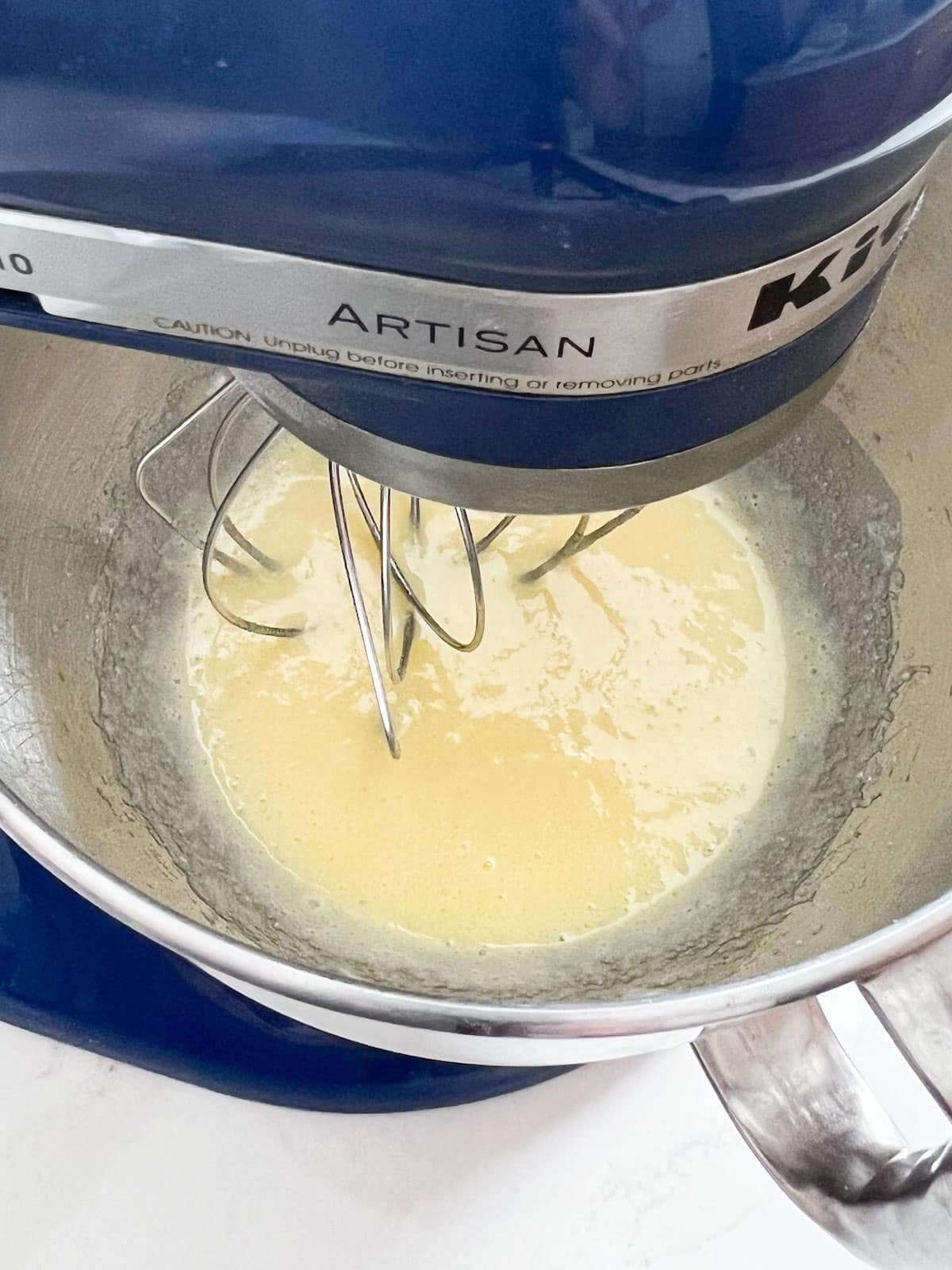 Lemon curd being mixed in a blue stand mixer.