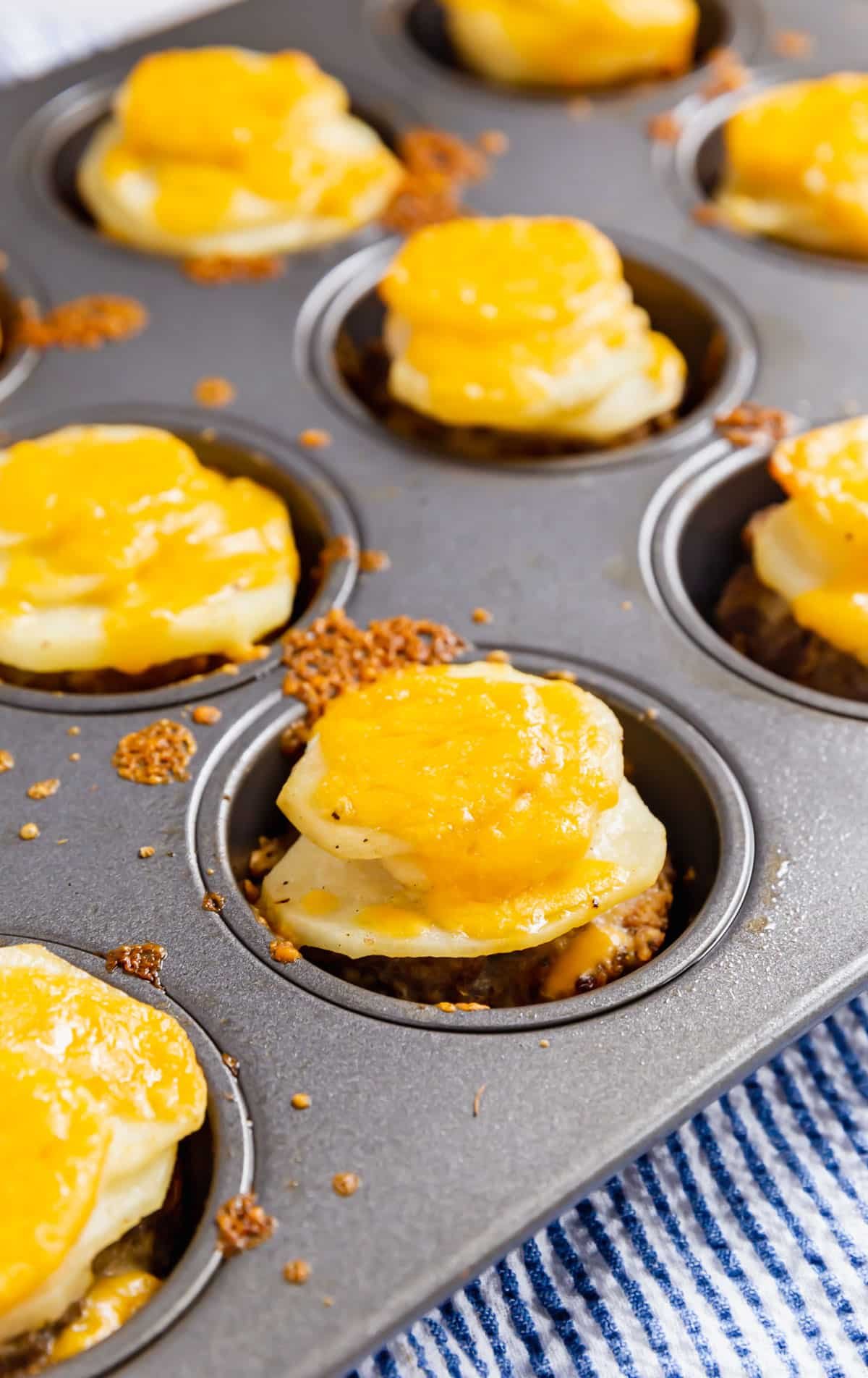 A side angle shot of the cheesy potatoes and meatloaves in a muffin tin.
