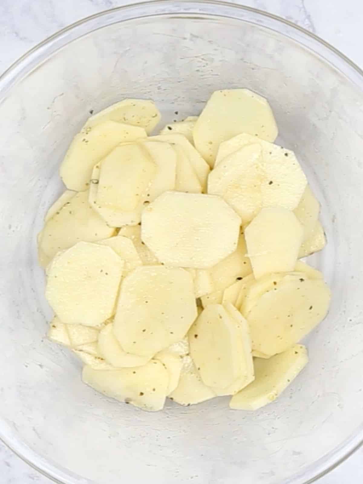 Seasoned sliced  potatoes in a glass bowl.