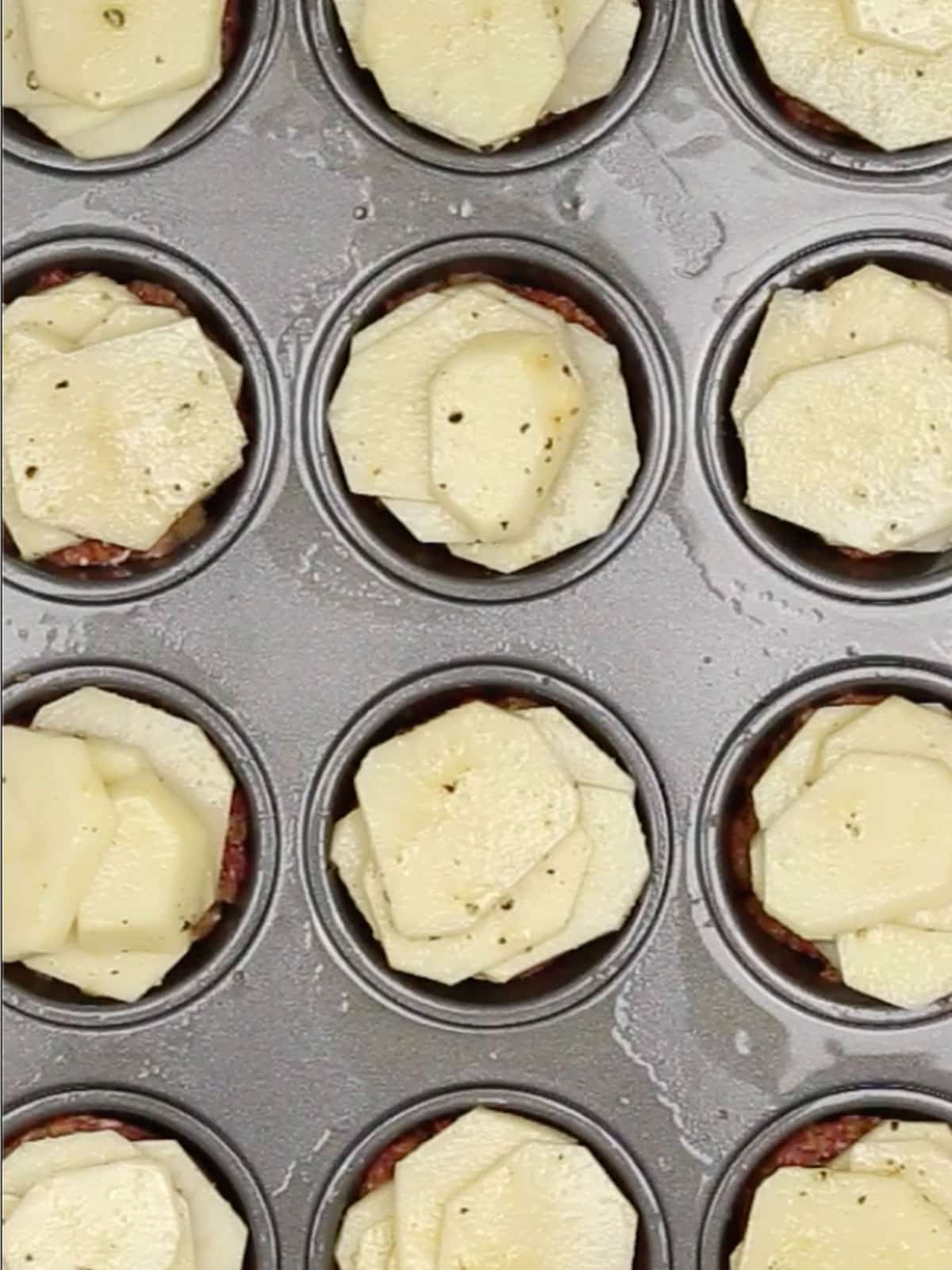 The mini meatloaves topped with seasoned sliced potatoes in a muffin tin.