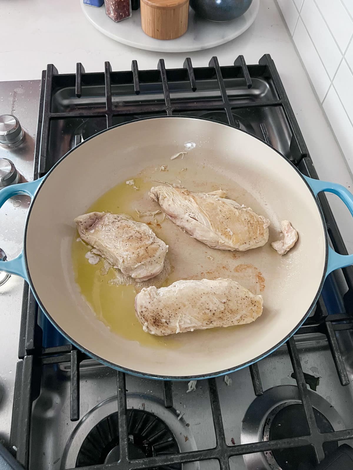 Chicken breasts being seared in oil in a blue pan on a stove.