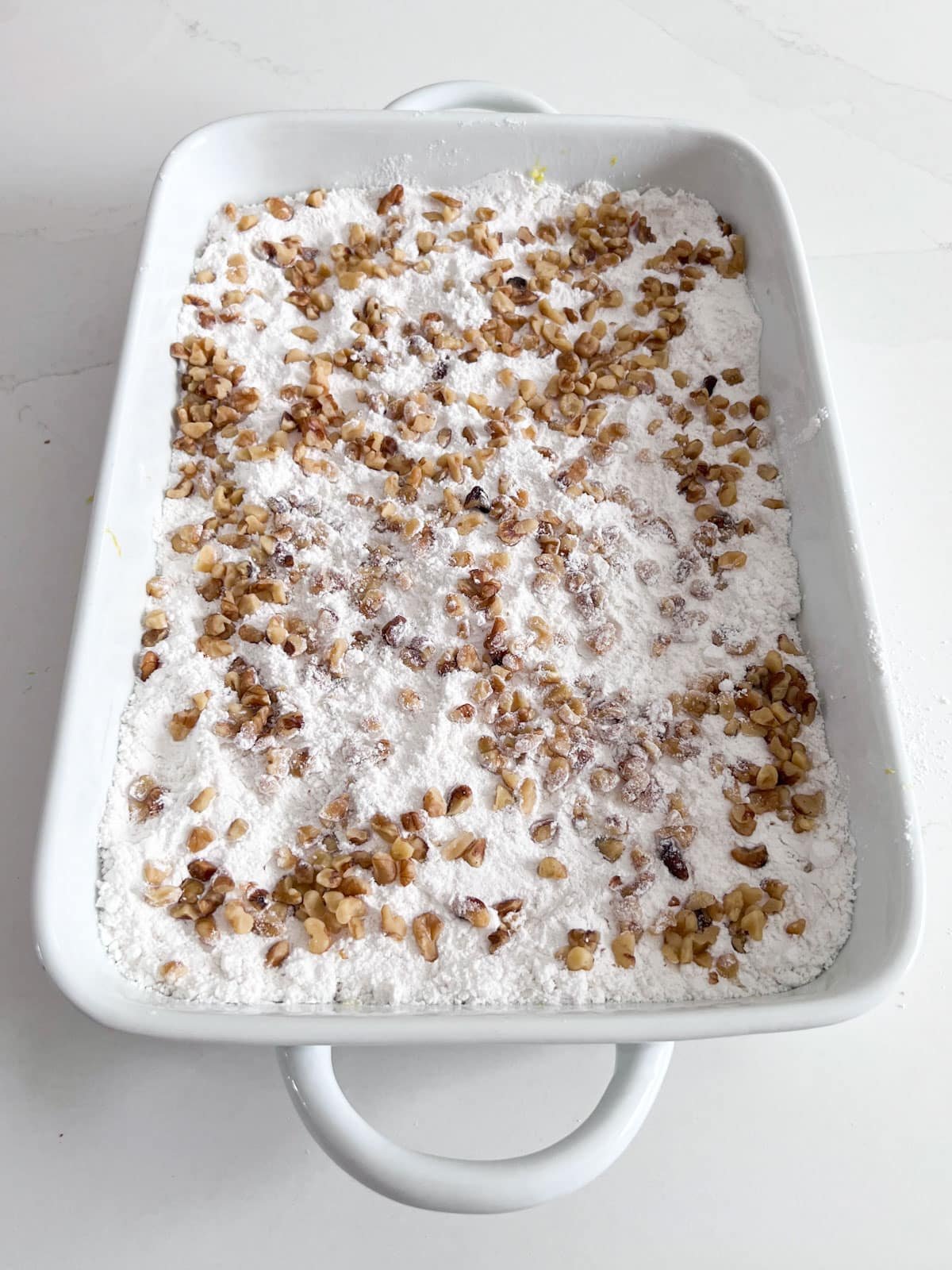 The cake pan with the even layer of cake mix on top and chopped walnuts sprinkled on that.