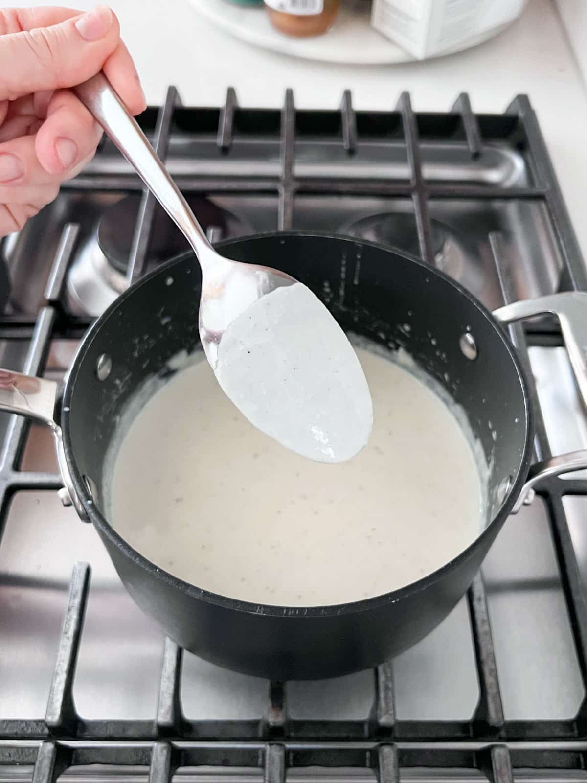 Thickened sauce in the pan with a spoon in front of it showing how the sauce coats the back of the spoon.