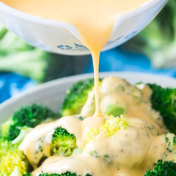A white pan pouring cheese sauce over a bowl of steamed broccoli.