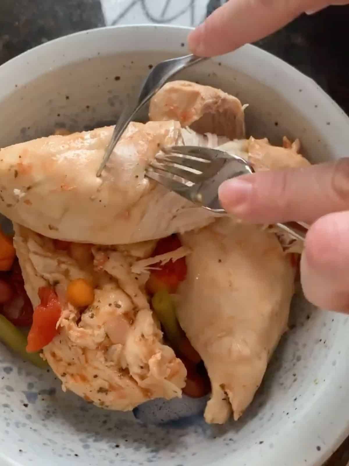 Hands shredding chicken with forks in a gray bowl.