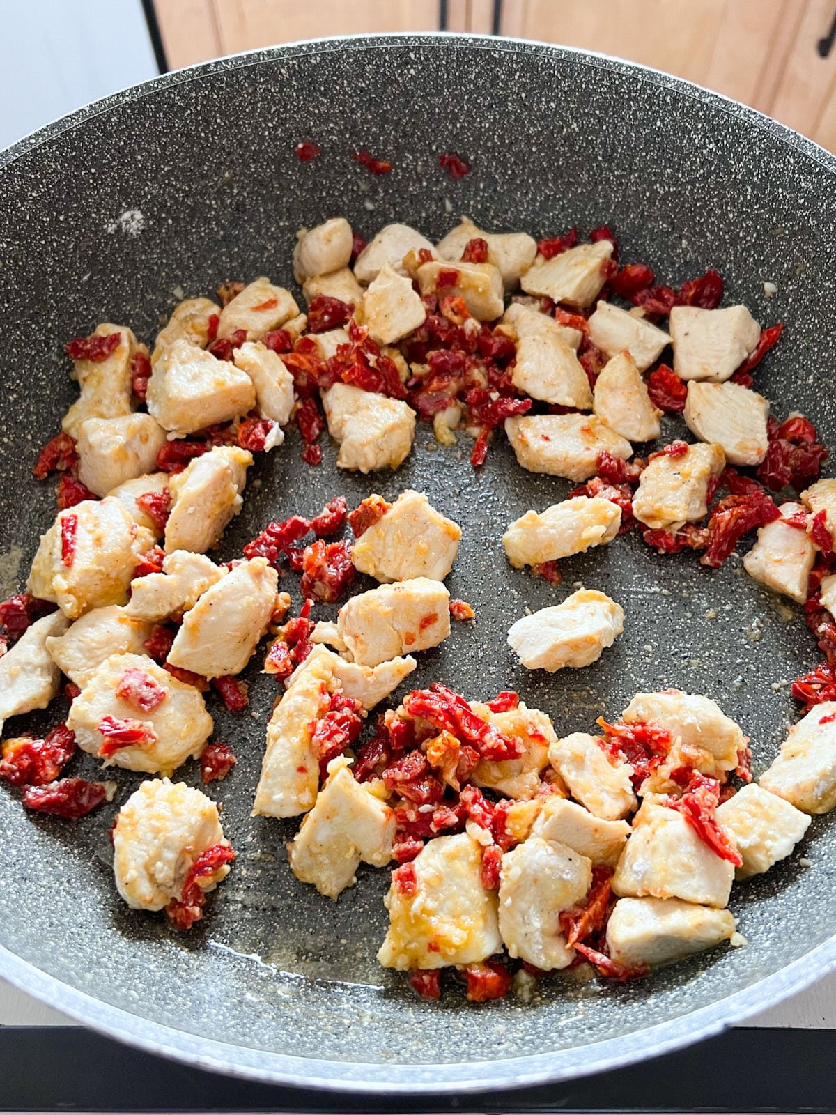 Cooked chicken in a skillet with sun-dried tomatoes and garlic.