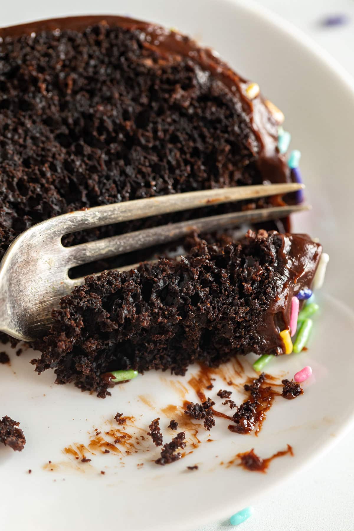A close up of a fork cutting a bite of a slice of chocolate cake.