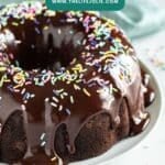 Chocolate bundt cake with chocolate ganache dripping down the sides and sprinkles on top with a teal napkin behind it.