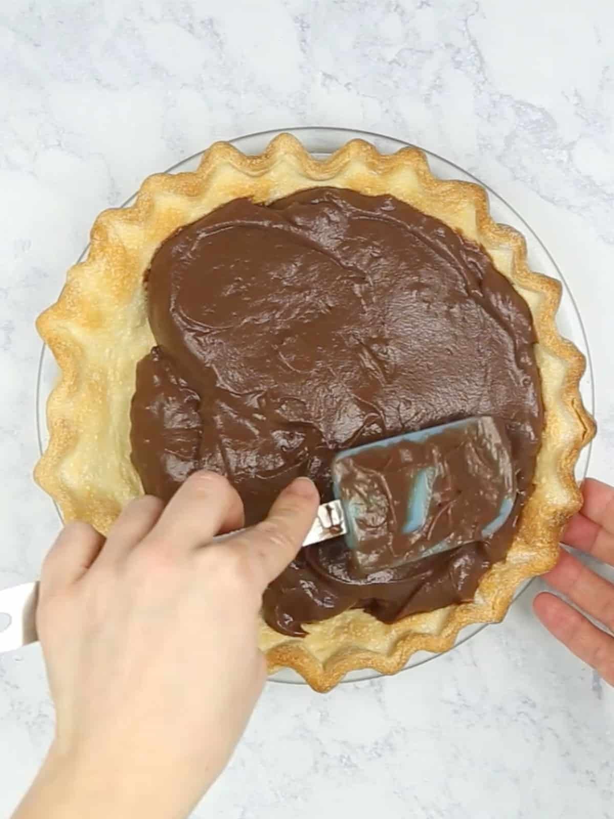 Chocolate pudding being spread in a baked pie crust.
