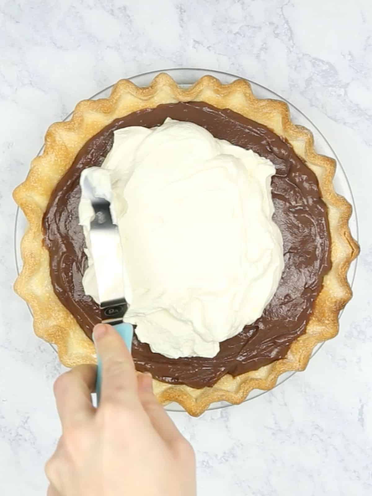Whipped cream being spread onto the chocolate pie.