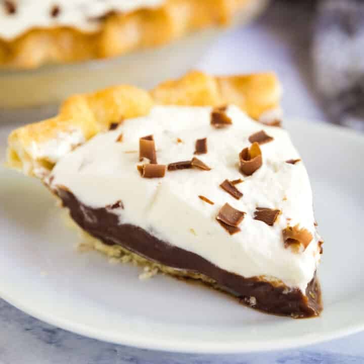 A close up image of a slice of chocolate pudding pie on a white plate with the rest of the pie behind it.