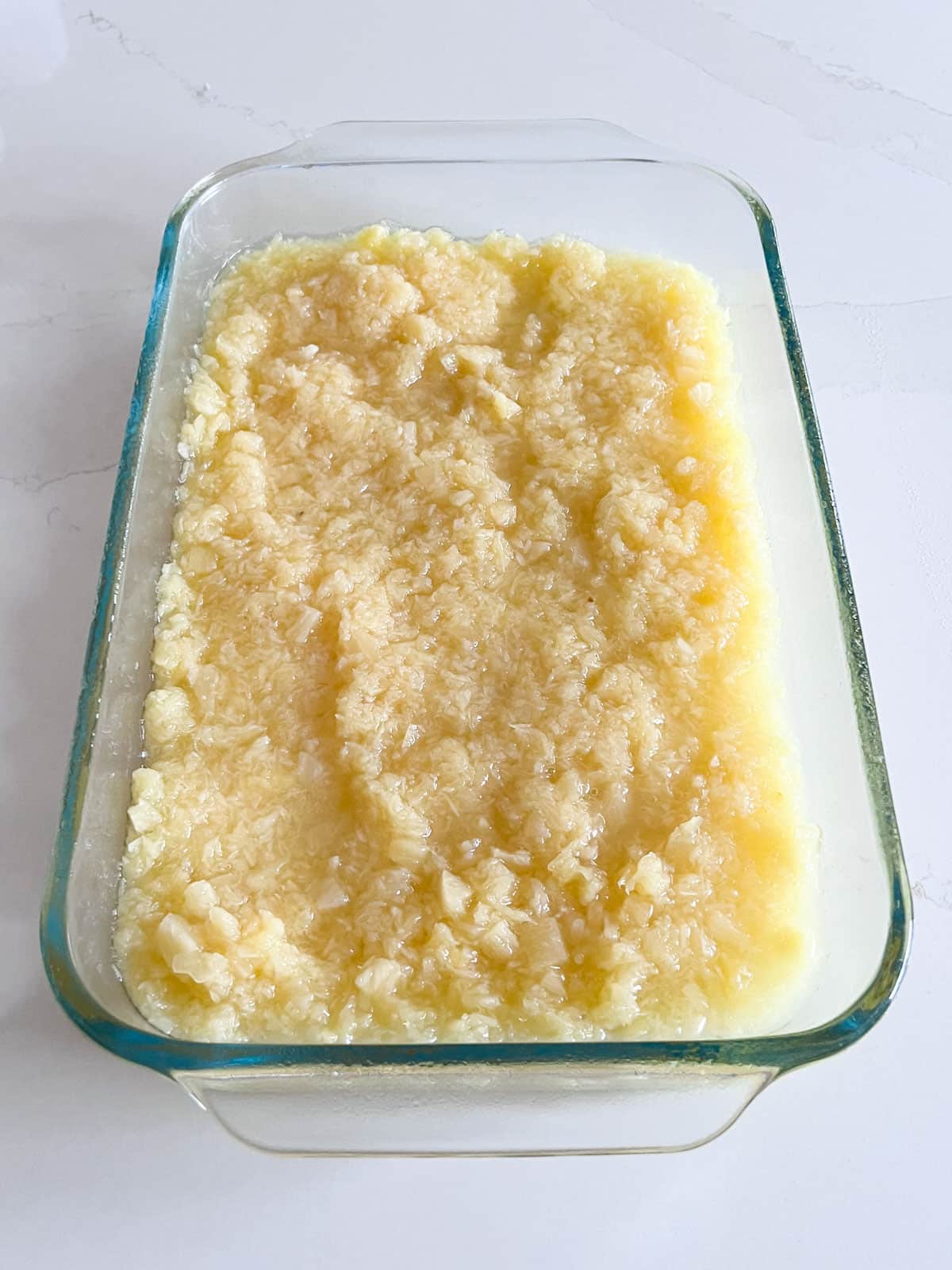 A clear glass baking pan with crushed pineapple spread along the bottom of it.