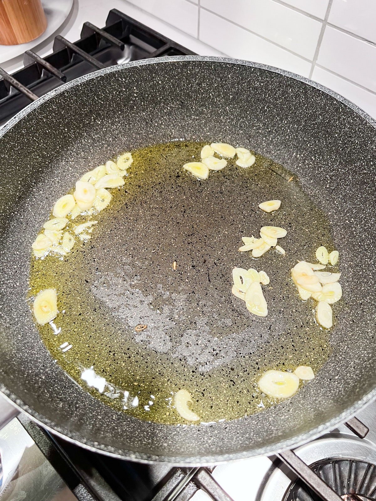 A sauté pan with hot oil and sliced garlic in it.