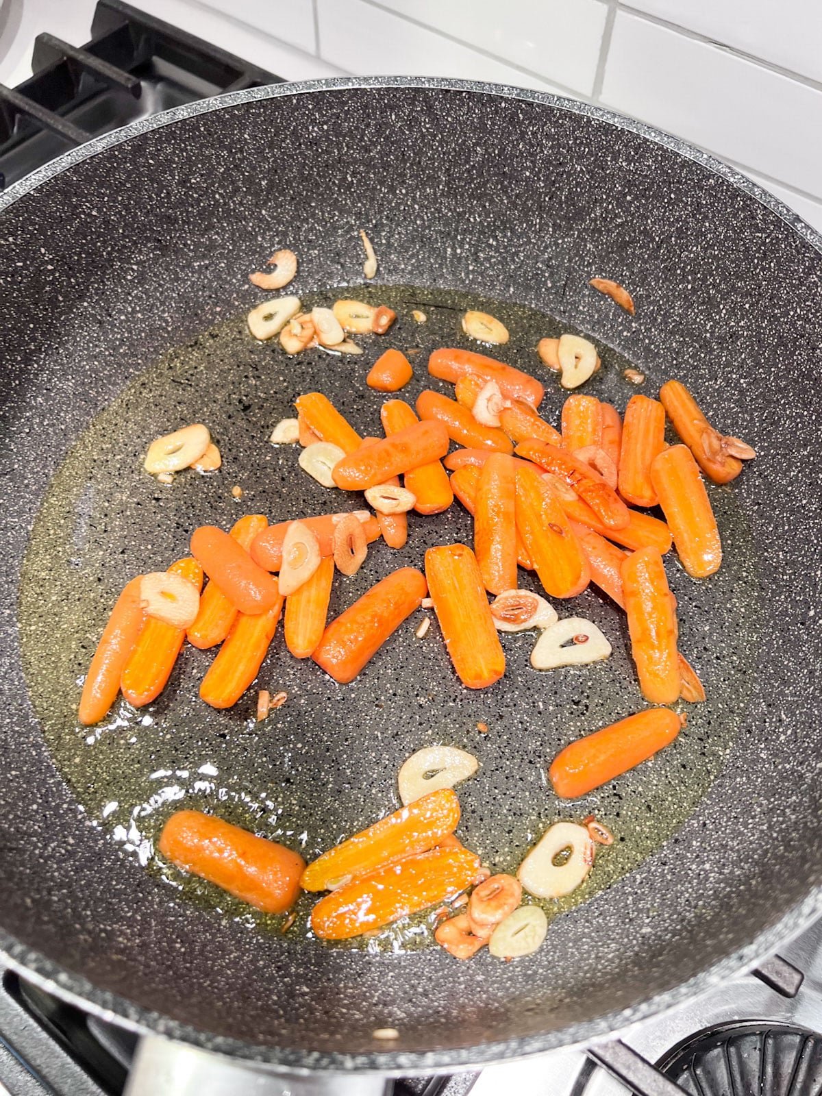 A sauté pan with carrots added to the hot oil and sliced garlic in it.