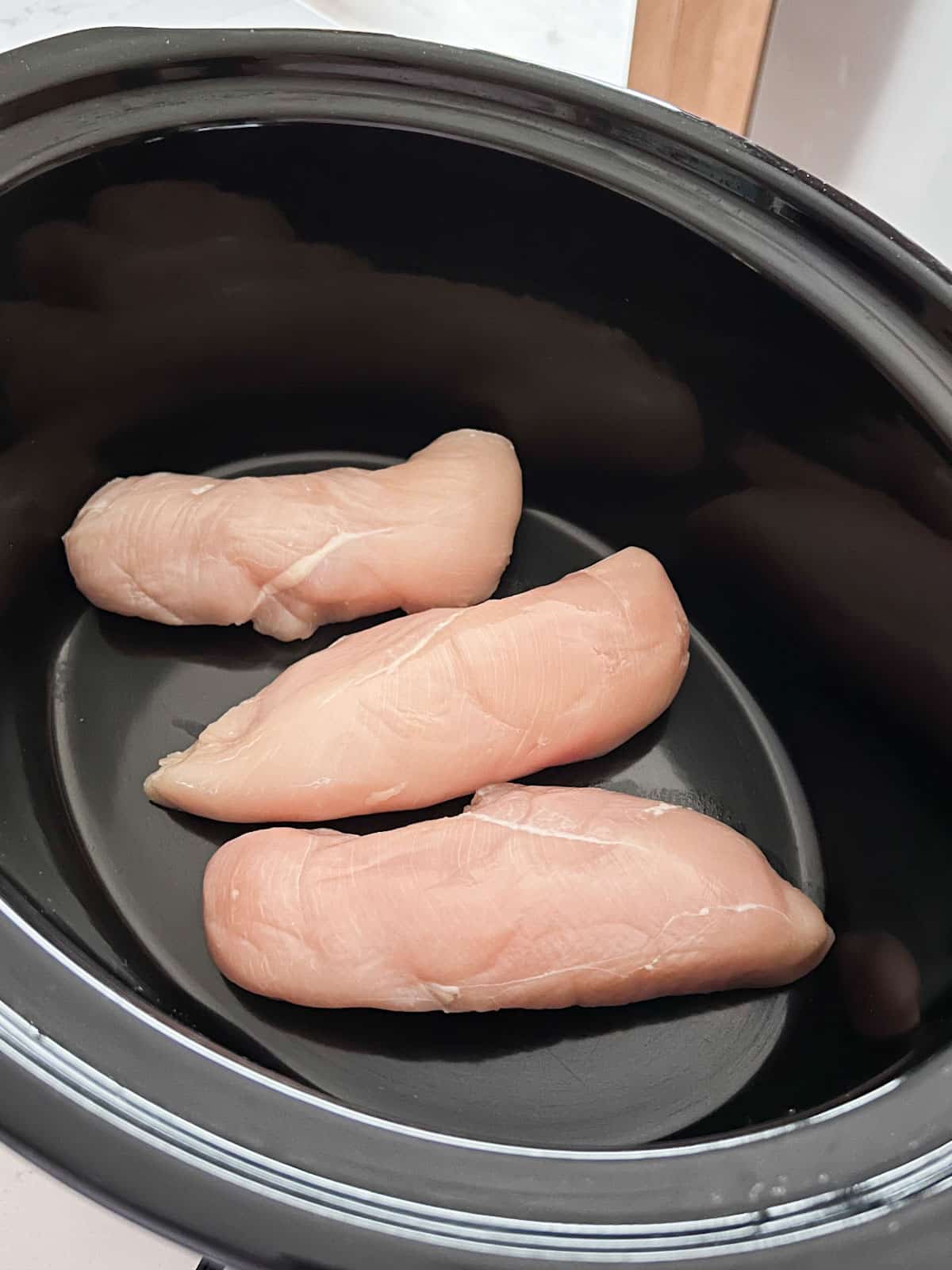 3 raw chicken breasts in a crockpot.