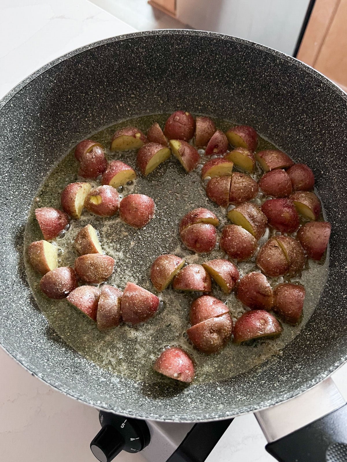 Partially cooked potatoes in a greased skillet cooking.