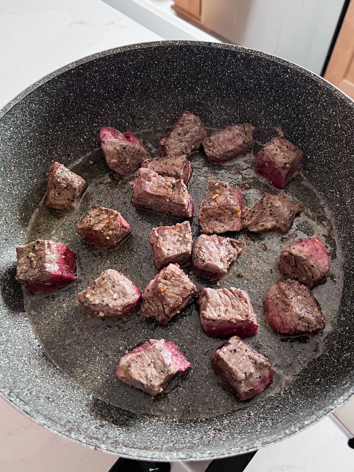 Partially cooked beef chunks cooking in a skillet.