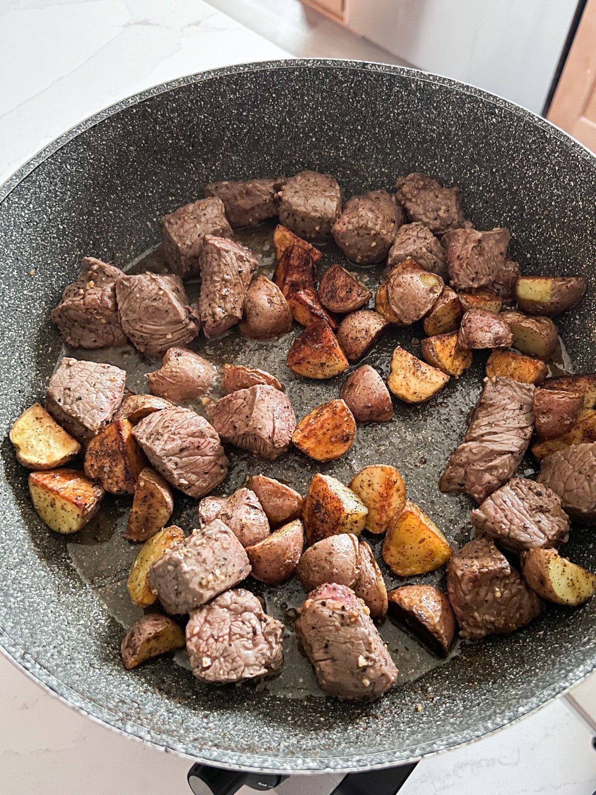 Potatoes added to the skillet of cooked beef.