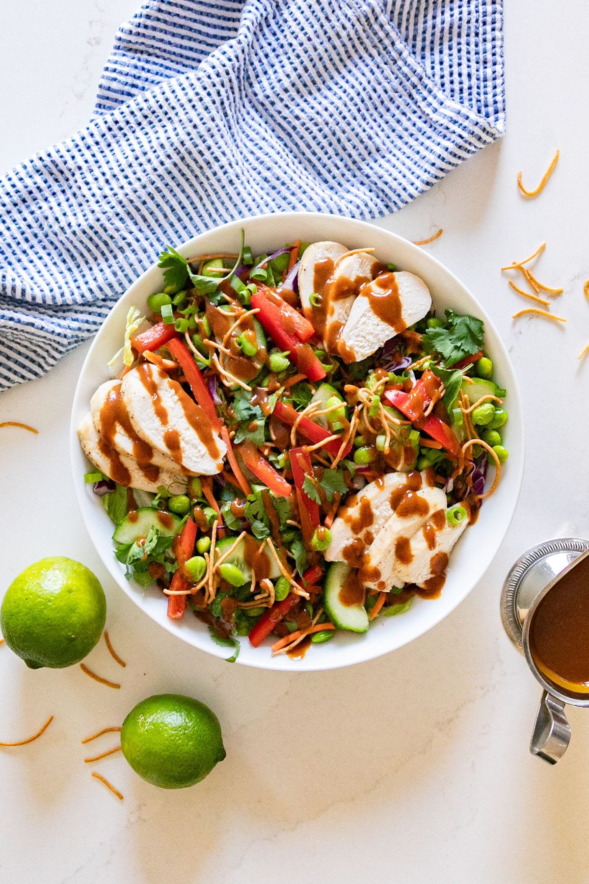 An overhead image of a crunchy asian salad with lines, blue napkin and dressing around it.