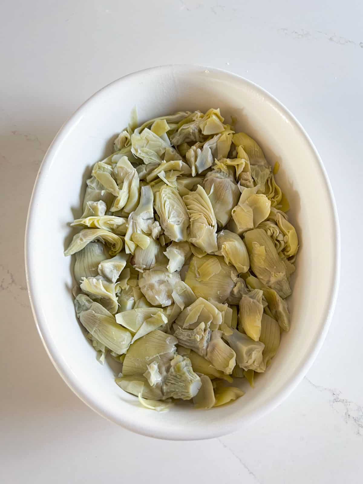 A layer of artichokes in a white baking dish.