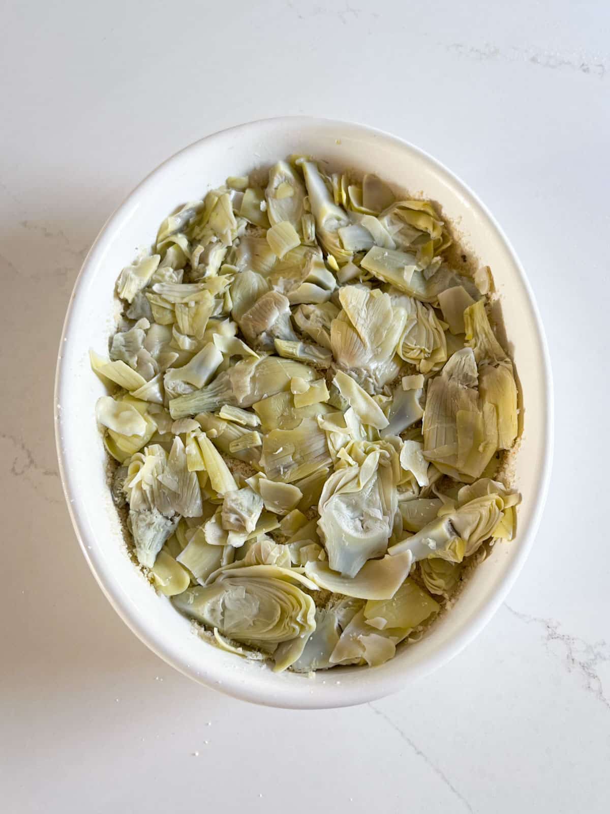 Another layer of artichokes in a white baking dish.