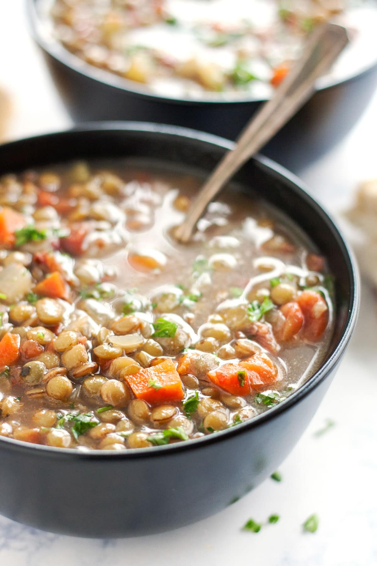 A close up image of the sde of a bowl of lentil soup with a spoon in it.