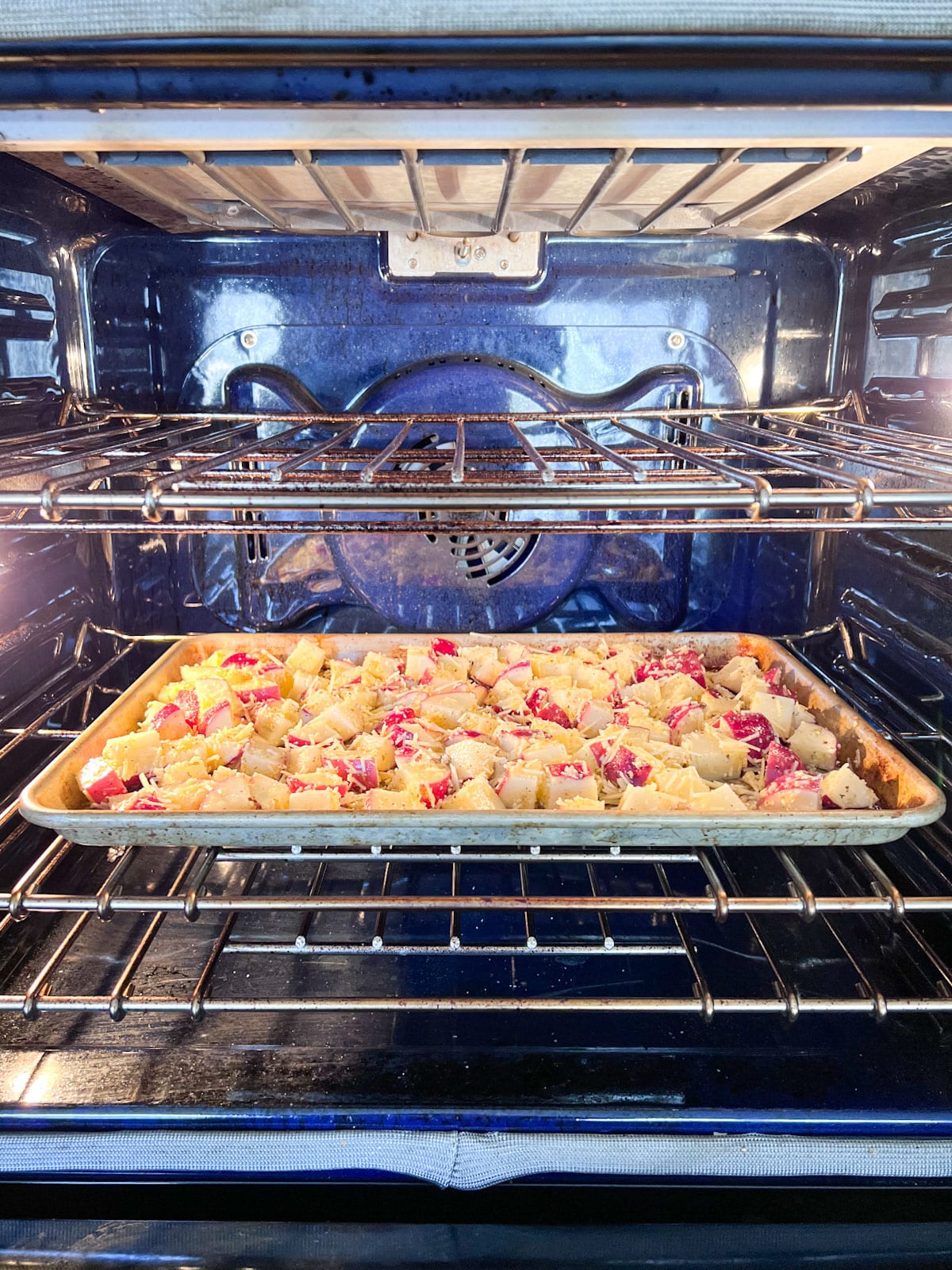 A sheet pan of potatoes in the oven about to be baked.