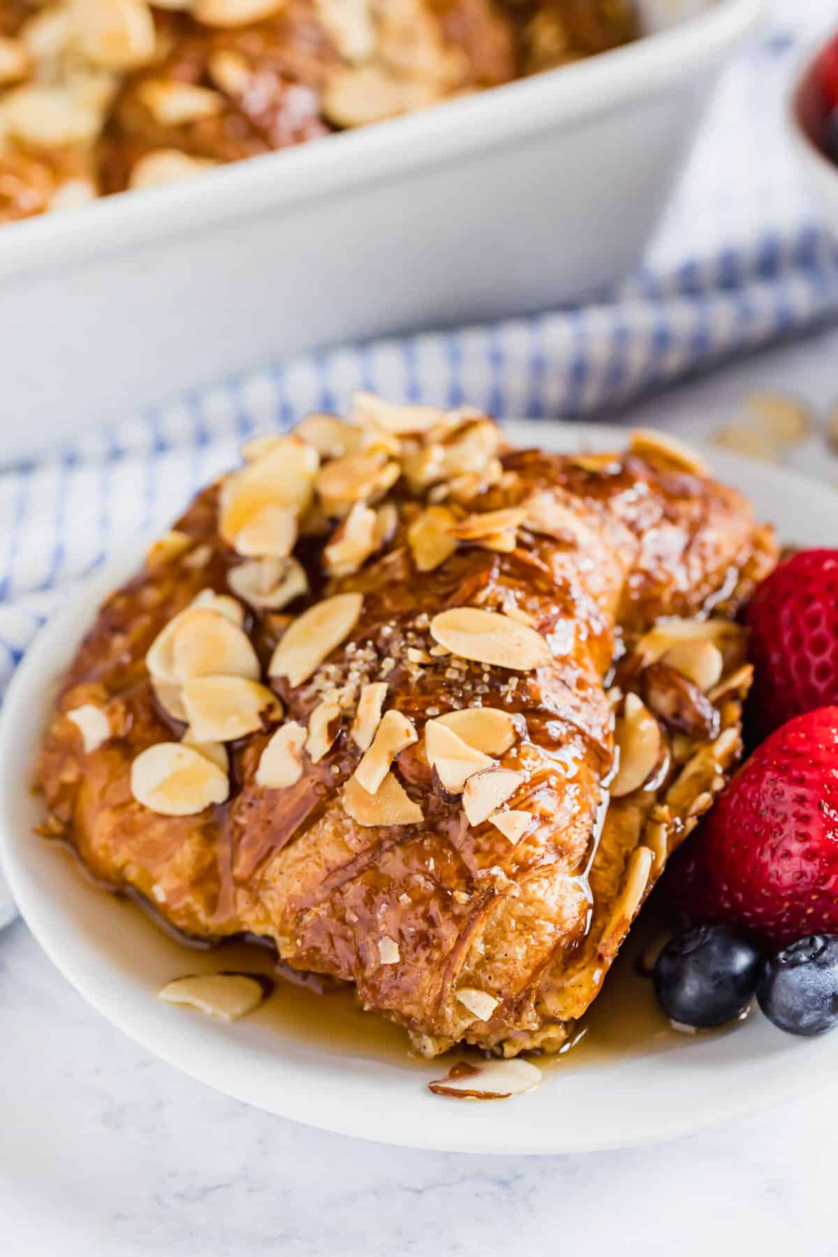 Croissant Baked French toast on a white plate covered in syrup with fresh berries on the side.