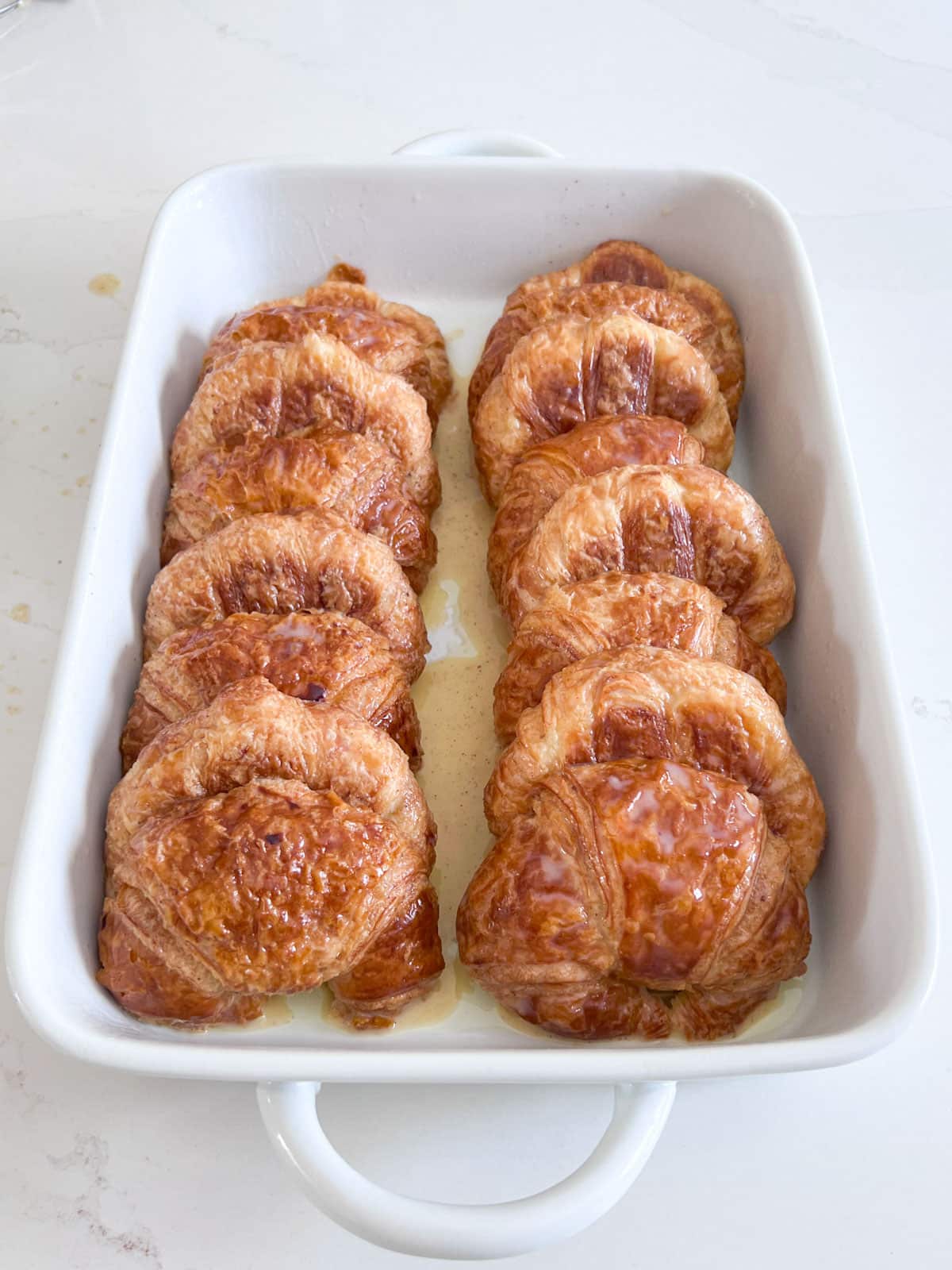 Shingled croissant halves in a white baking pan with the remaining custard poured over them.