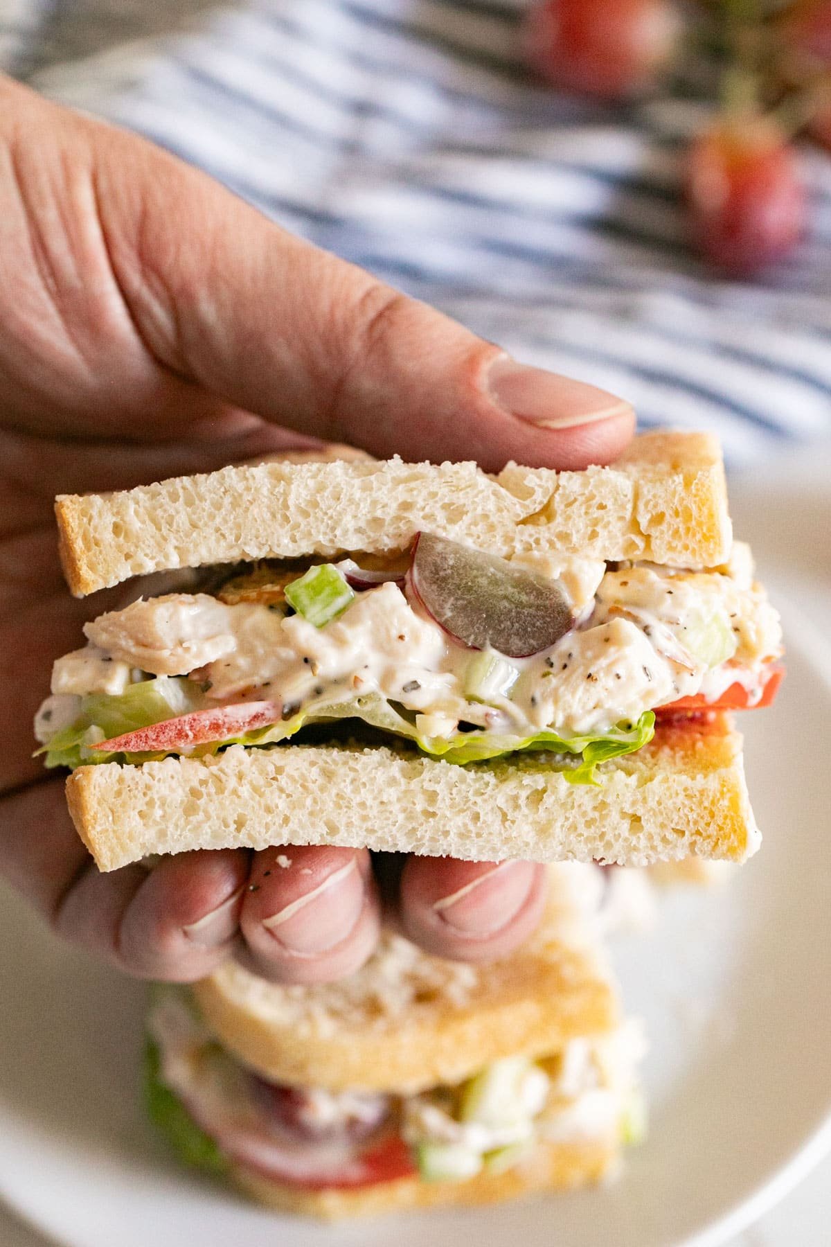 A hand hold a half chicken salad sandwich revealing the inside of it