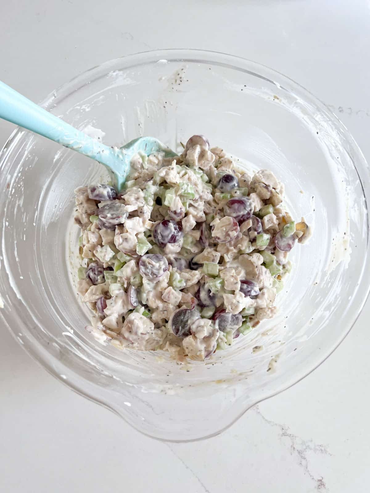 Chicken salad mixed together in the bowl with a blue spoon in it.