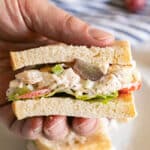 A hand holding a half chicken salad sandwich revealing the inside of it
