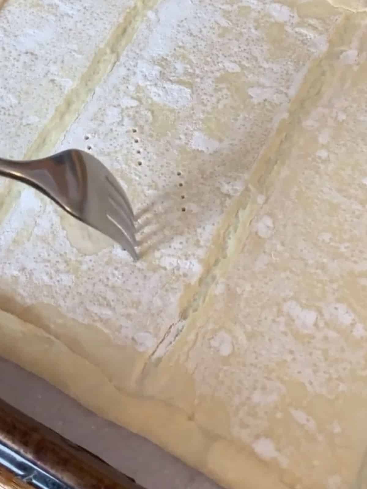 A fork piercing into a raw puff pastry sheet.