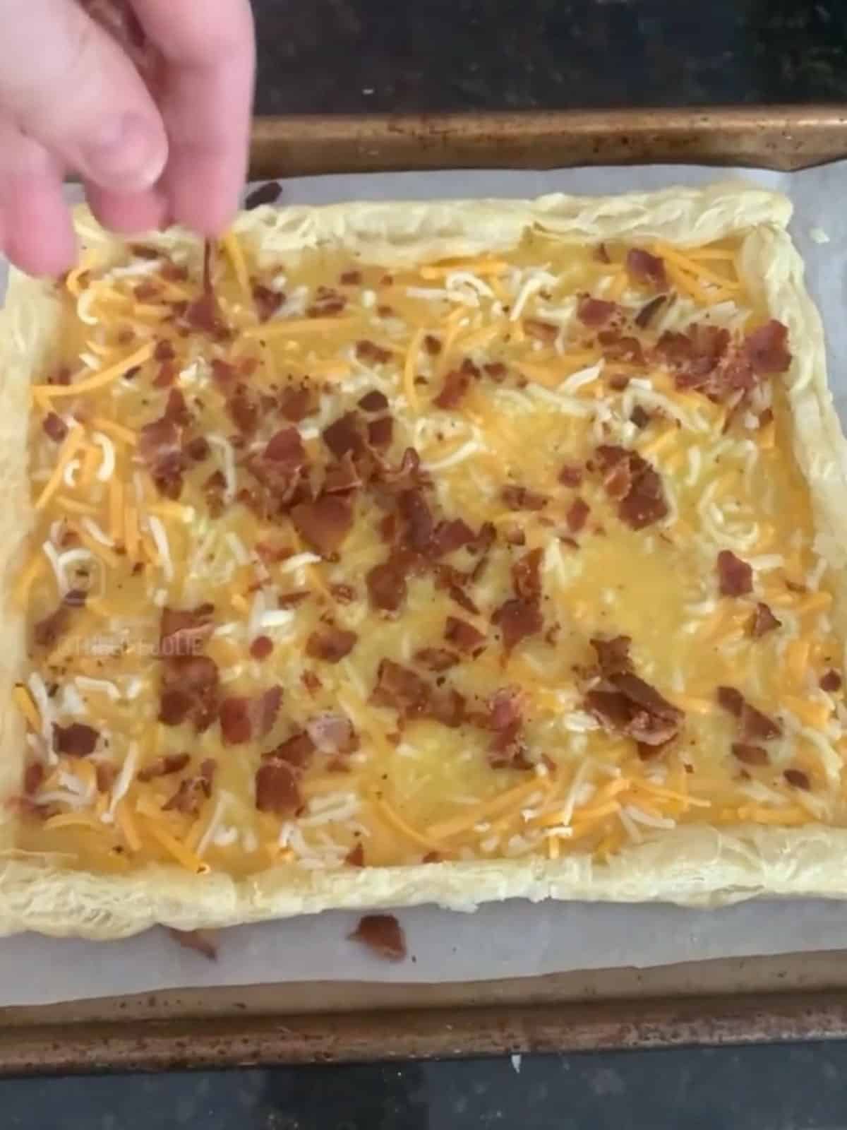 Bacon being sprinkle onto the egg mixture in the puff pastry crust.