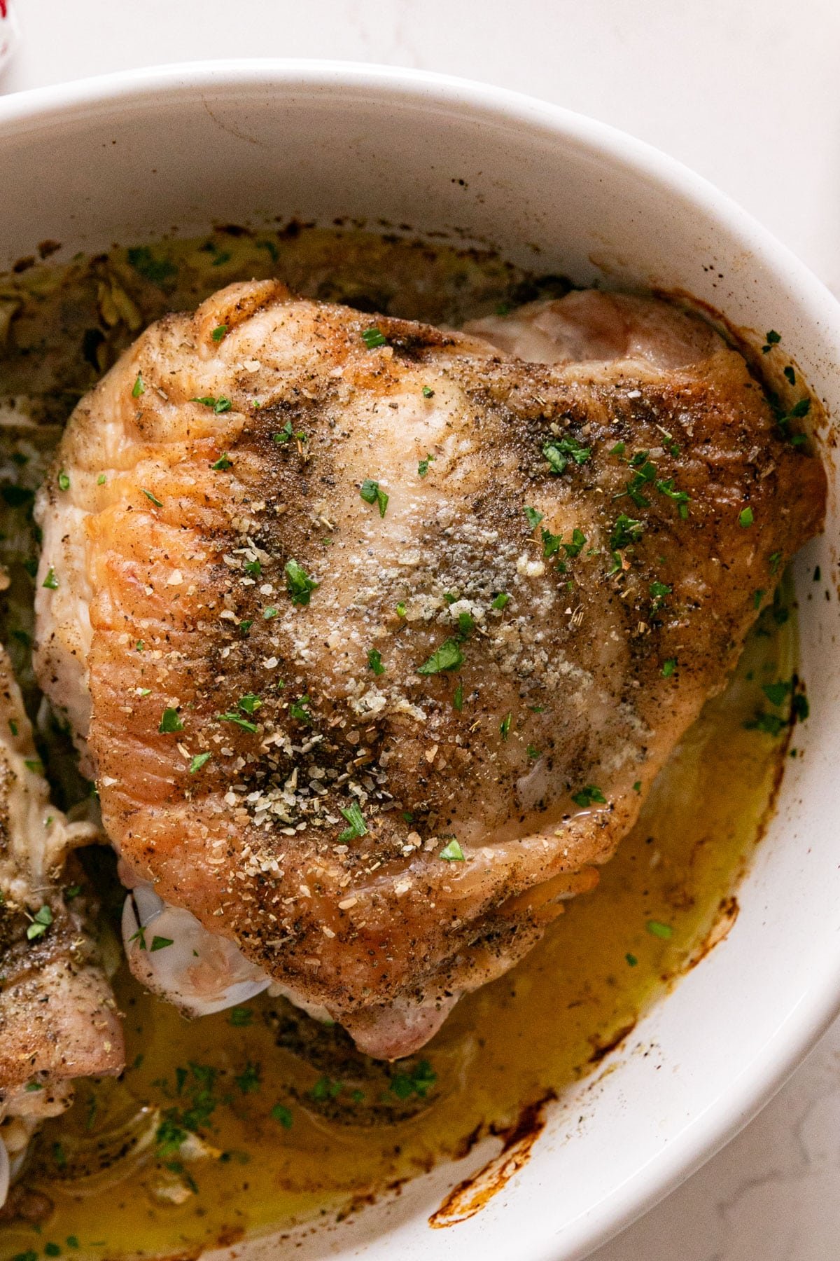 A close up overhead shot of a perfectly roasted turkey thigh in a white oval baking pan.