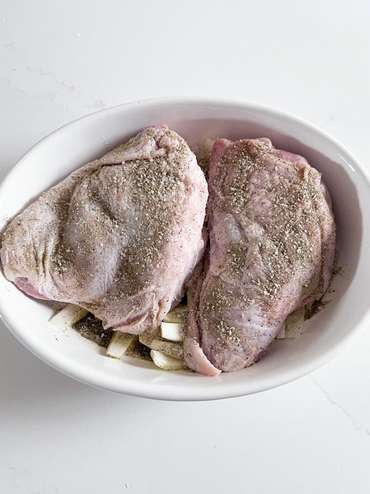 Raw turkey thighs with seasoning on them in the white oval baking pan.