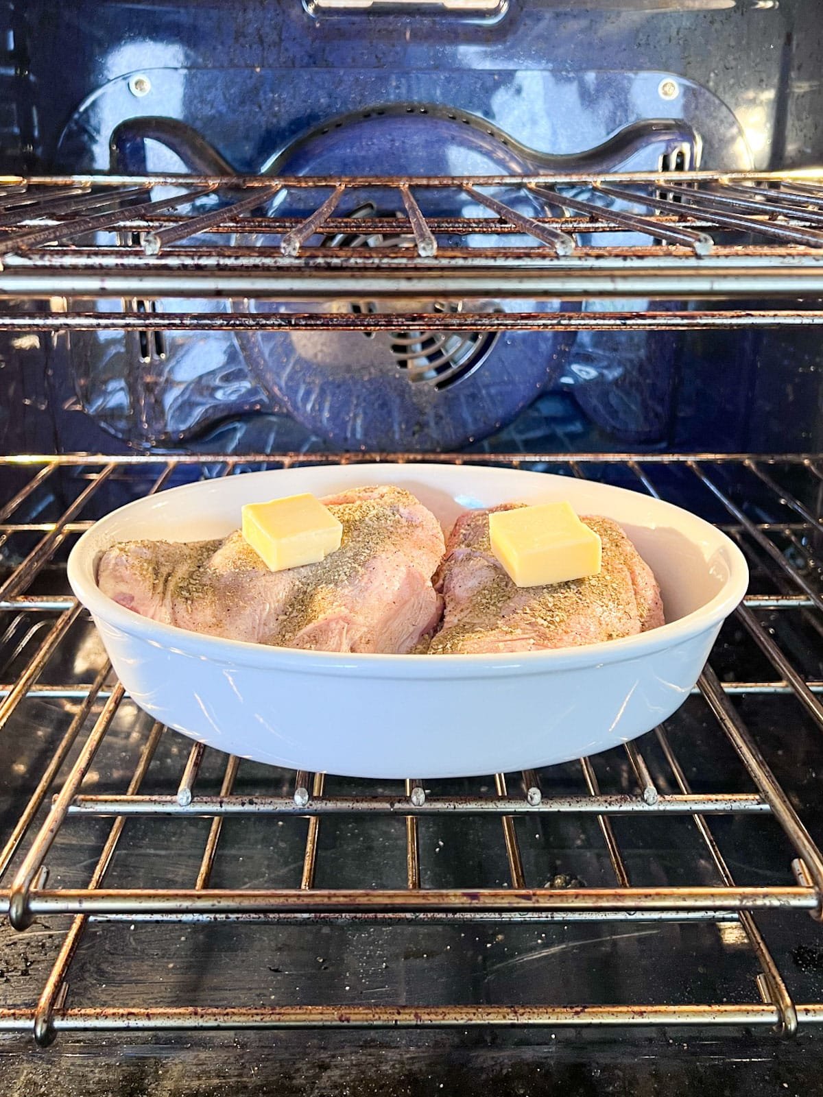 Turkey thighs in a white oval baking pan in the oven about to cook.