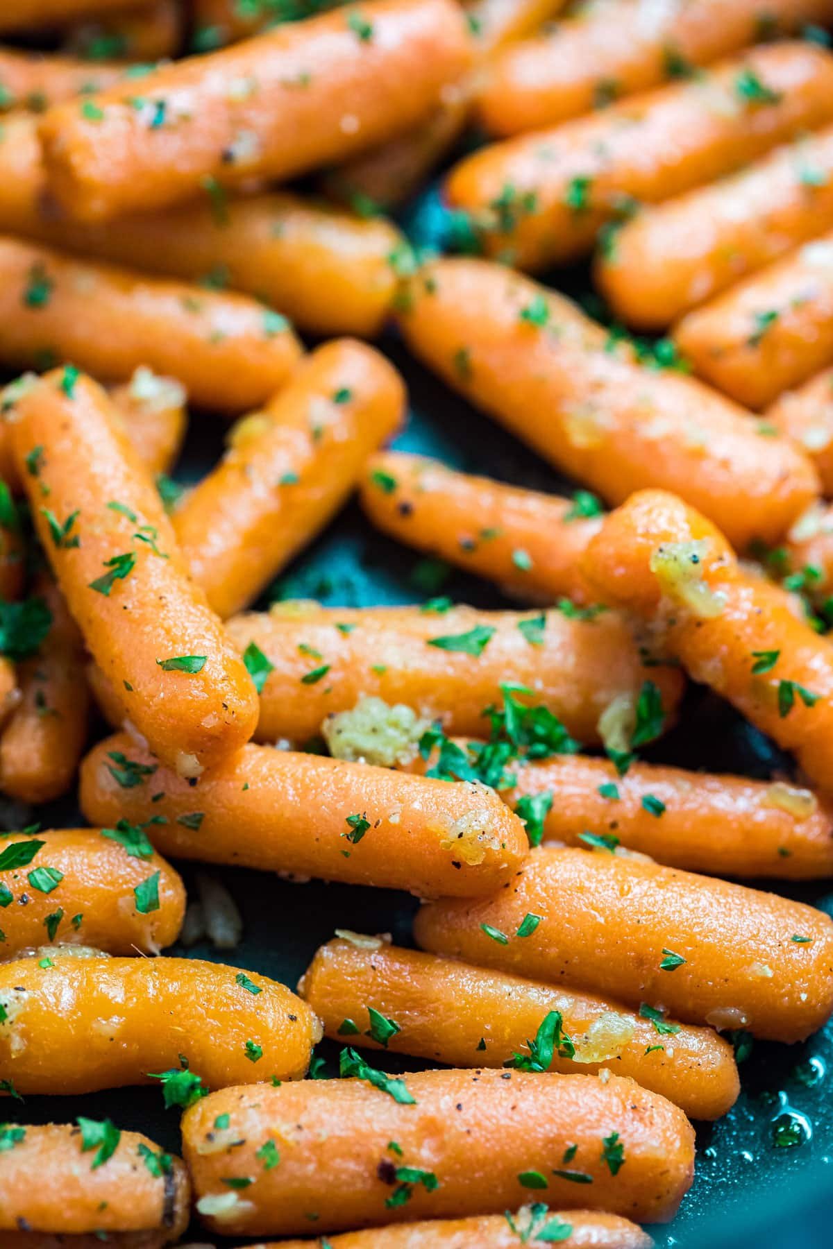 A close up side angle shot of carrots with parsley in a pan.