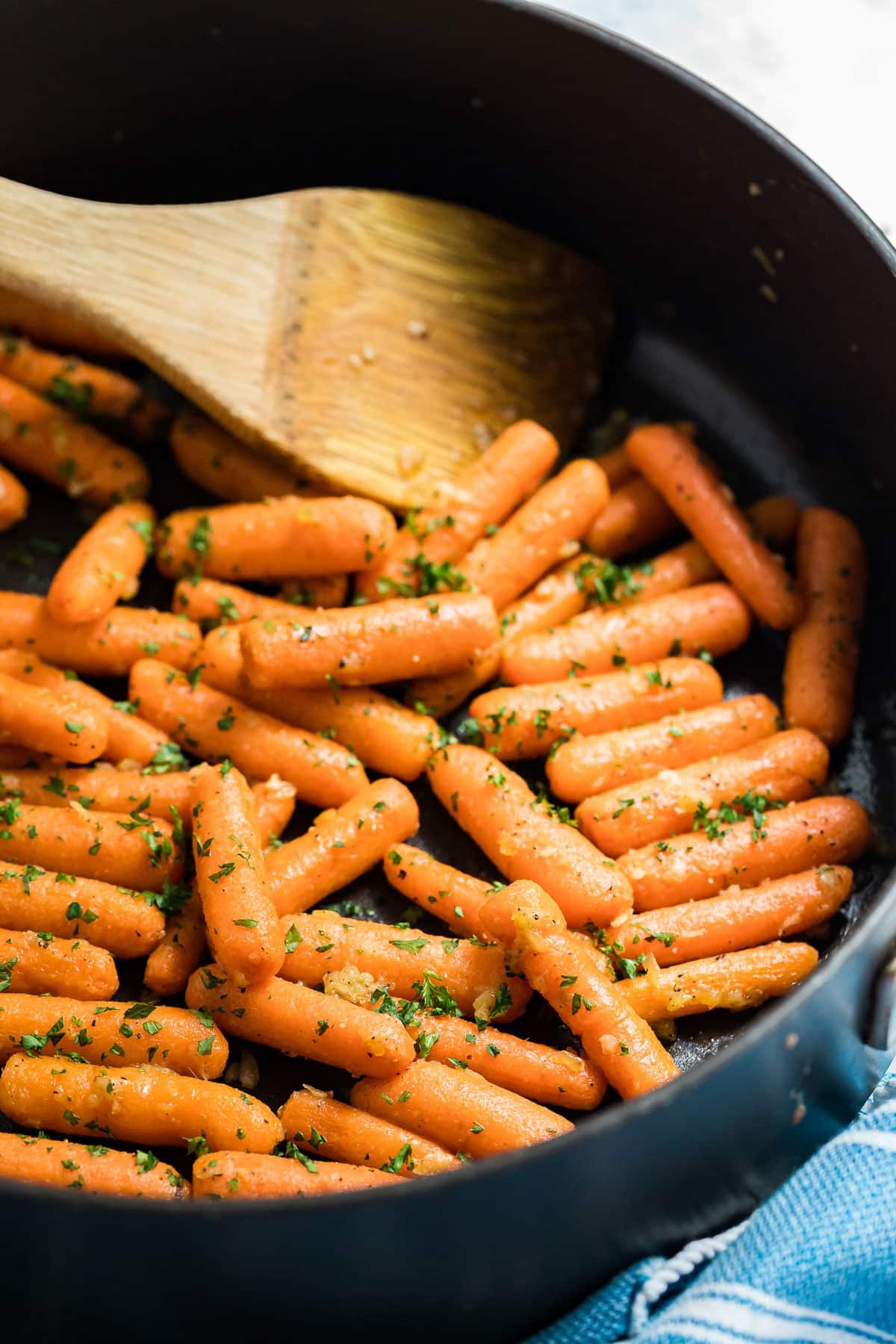 The side of a pan of sauteed carrots with a wooden spoon in it.