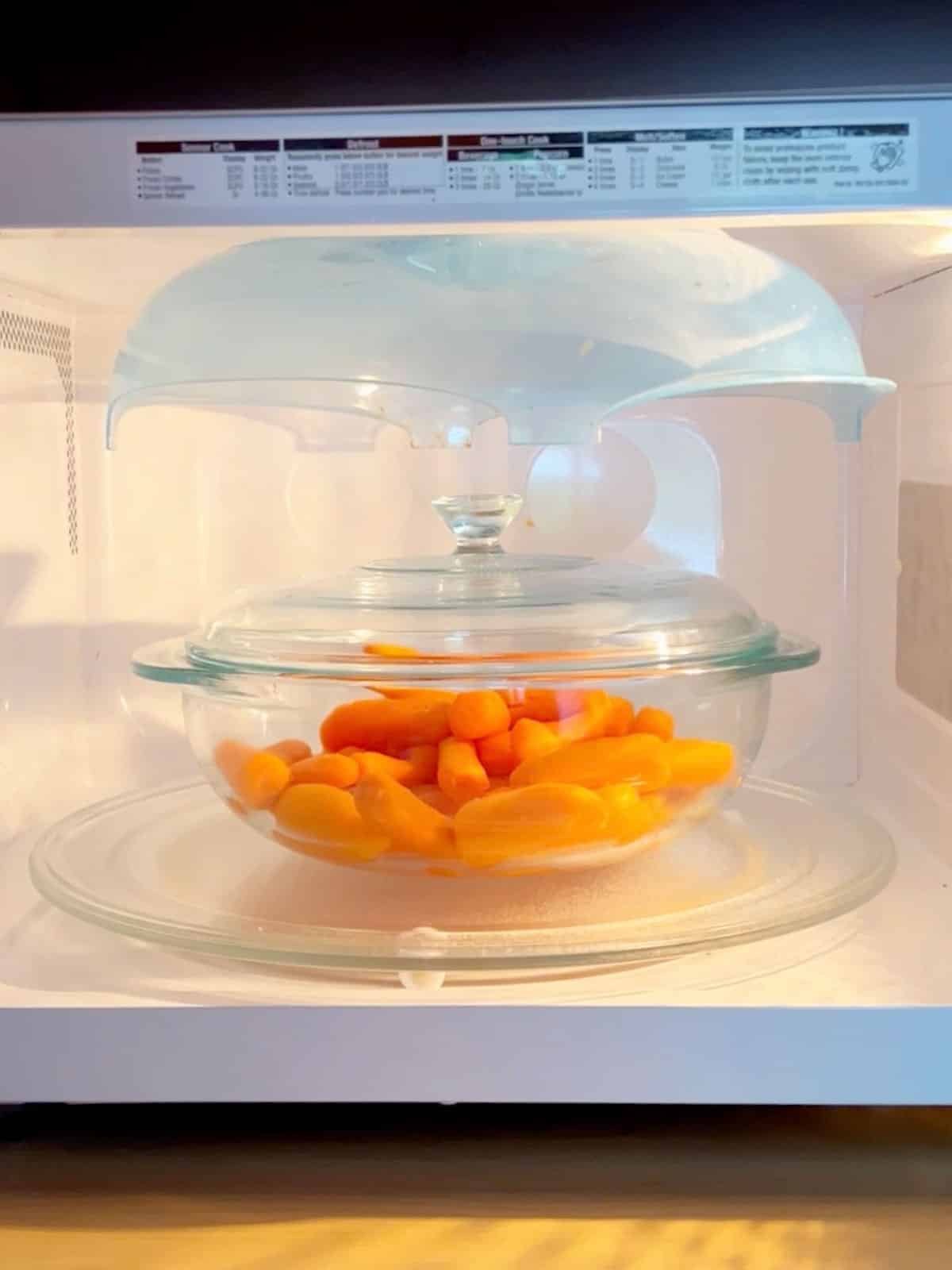 A covered bowl of carrots in a microwave.