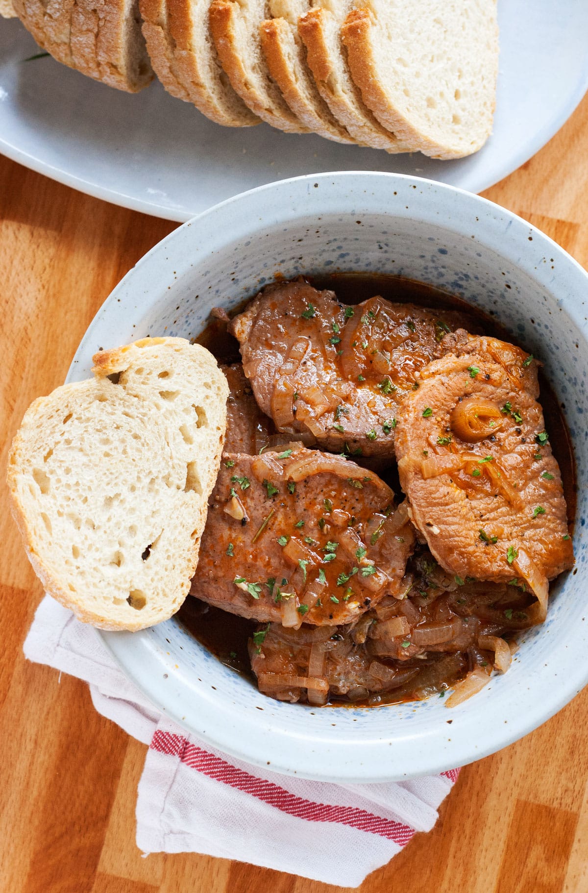 An overhead image of a gray bowl of drunken pork chops with bread on the side.