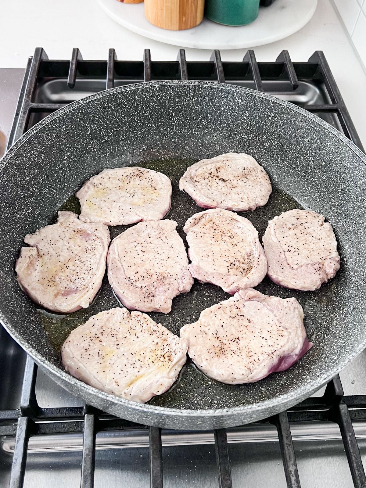 Seasoned thin pork chops browning in a large skillet on the stove.