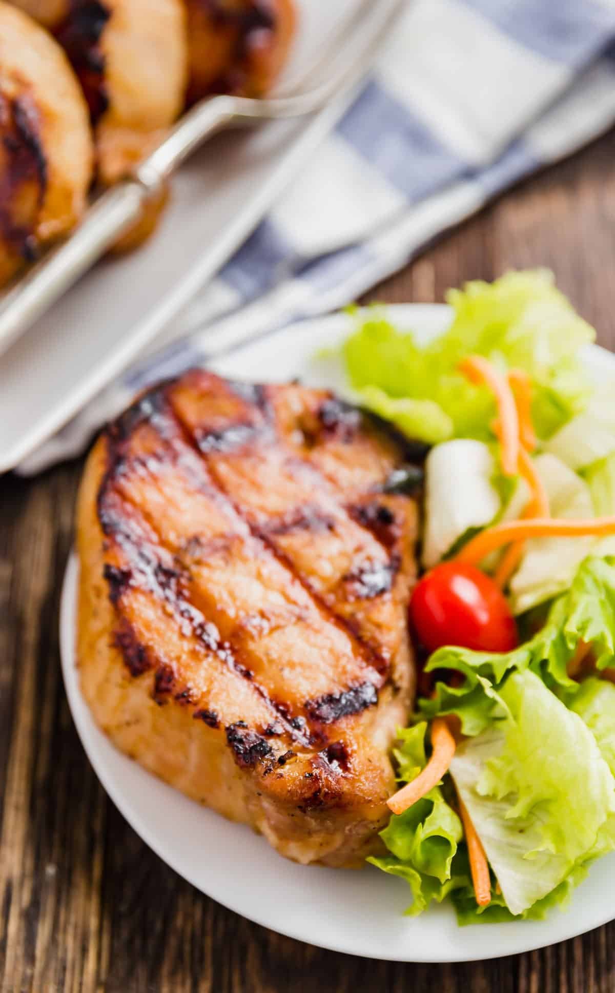 A pork chop that's been grilled on a plate with salad.