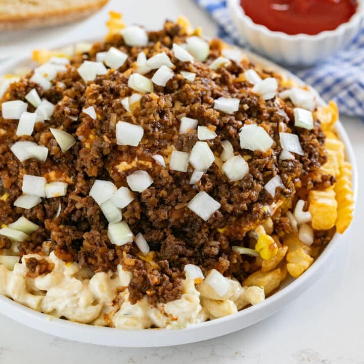 A garbage plate with a blue towel, ketchup and Italian bread in the background.