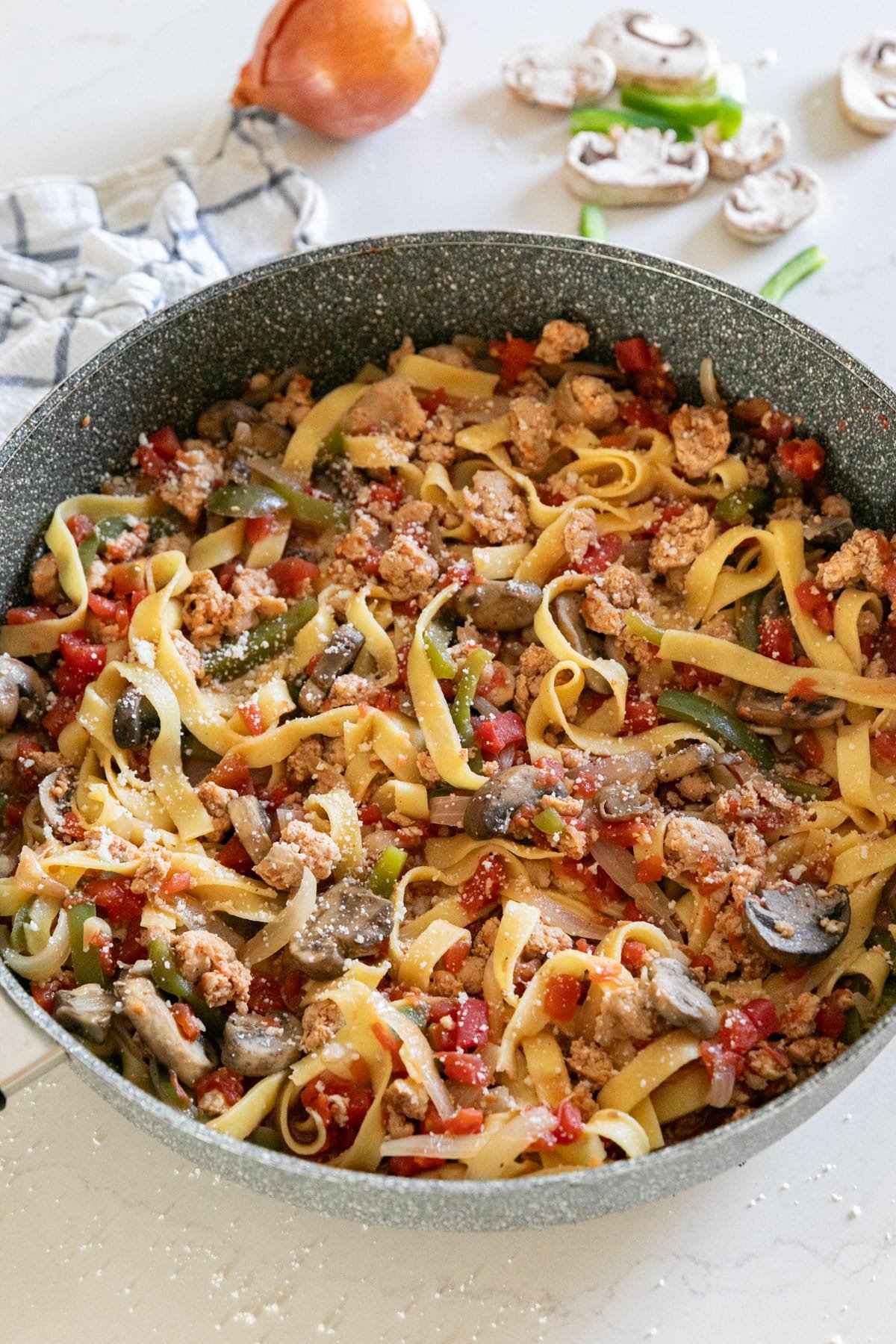 A pan of peppers onions and sausage pasta with veggies and a napkin behind it.