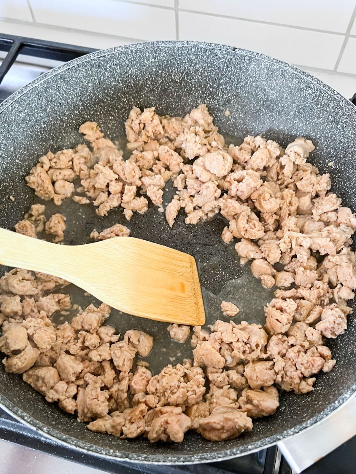 A wooden spoon deglazing the pan of sausage with white wine.