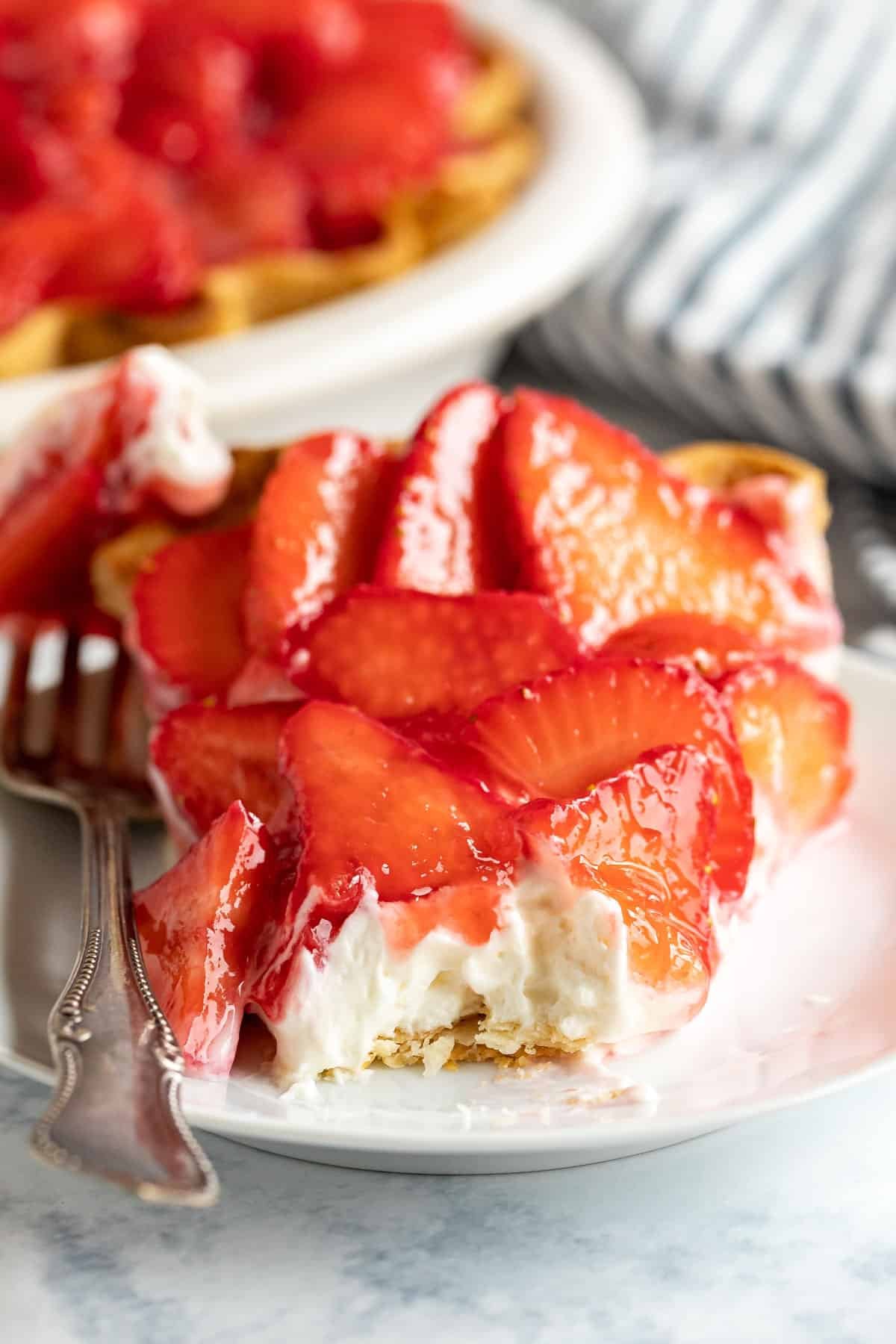An image looking straight at a slice of strawberry cream cheese pie with a bite taken off revealing the creamy filling with the strawberries on top.