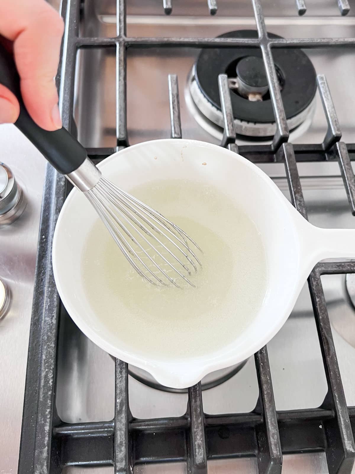 Glaze mixture thickening on the stove with a whisk in it.